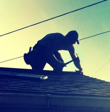 Josh kneeling on a roof at sunrise, nail gun in hand